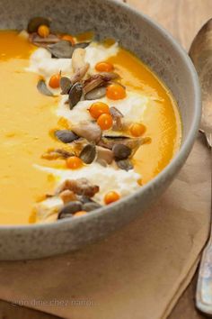 a bowl of soup with carrots, cream and nuts in it on a wooden table