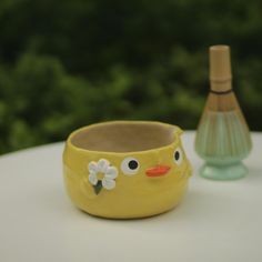 a yellow cup sitting on top of a white table next to a green glass bottle