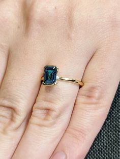 a woman's hand with a ring on it that has an emerald colored stone in the middle