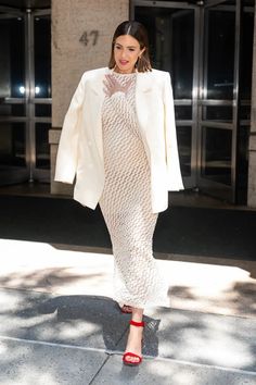 a woman in a white dress and jacket is walking down the street with her hand on her hip