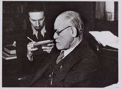 two men sitting at a table with papers in front of them and one man holding a book