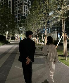 a man and woman are walking down the street at night in front of tall buildings