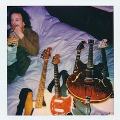 a man laying in bed next to three guitars