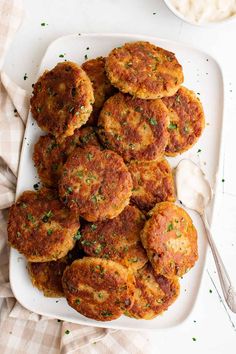 several crab cakes on a white plate with a bowl of cottage cheese in the background