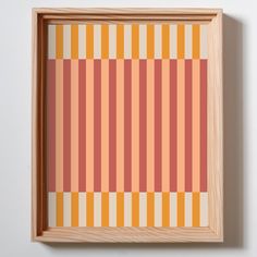 an orange and pink striped wall hanging in a wooden frame