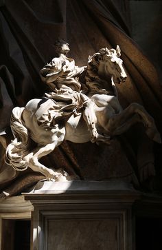 a statue of a man riding on the back of a white horse in front of a wall