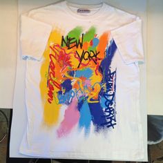 "Here is a beautifully handpainted white t-shirt from Bleu Dstrkt with a New York logo and heavy, intricate splatter paint work that is reminiscent of American Abstract Expressionism, in what appears to be a Men's L(arge). This is a vintage used item, in good used condition, with little/no sign of use or wear; there are no evident tears, rips, holes, loose threads or stains. Evident cotton or cotton/polyester mix fabric quality remains good and graphics are bright/sharp, like new and shirt appea Casual Paint Splatter T-shirt For Streetwear, Streetwear Paint Splatter Graphic Tee, Graphic Tee With Paint Splatter For Streetwear, Casual T-shirt With Paint Splatter For Streetwear, White Paint Splatter Crew Neck T-shirt, Urban Multicolor Graffiti Print T-shirt, White Paint Splatter Tops For Streetwear, White Short Sleeve T-shirt With Paint Splatter, Artistic White Tops With Custom Artwork