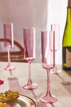 pink wine glasses and plates with grapes on a table next to bottles of wine in the background