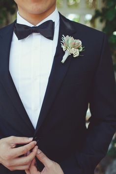 a man in a tuxedo adjusts his flower on the lapel of his suit