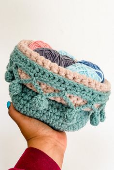 a hand is holding a crocheted basket with balls of yarn in the middle