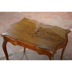 an old wooden table with glass top and ornate carvings on the side, sitting in a room