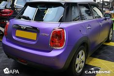 the back end of a purple mini car parked in a parking lot next to other cars