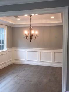 empty room with chandelier and hard wood flooring in the middle, white paneling on the walls