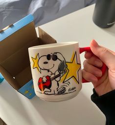 a hand holding a coffee cup with a cartoon character on it and a red handle