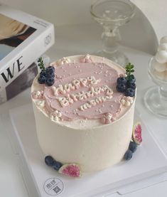 a birthday cake with blueberries and raspberries on the top is next to a book