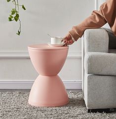 a pink stool with a coffee cup on it in front of a white wall and a plant