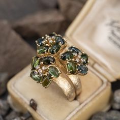 This ring by designer Vancox features three floral style cluster settings each accented with five (5), bezel set, round brilliant cut diamonds and five (5), prong set, oval cabochon cut natural tourmaline. The ring measures 22.9mm at the top, rises 11.0mm above the finger, tapering to 4.8mm wide and 0.7mm thick at the base of the shank. The ring is currently size 10. Elegant Diamond Cluster Ring With Gemstone Accents, Elegant Three Stone Tourmaline Jewelry, Diamond Flower Ring, Diamond Flower, Size 10 Rings, October Birth Stone, Floral Style, Flower Ring, Oval Cabochon