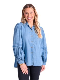 A smiling person with long hair stands against a white background, wearing the Oxford - Denim Chambray shirt featuring signature gold buttons and black pants. They accessorize with gold hoop earrings and a bracelet, completing their stylish look. Clothing Pieces, Cotton Poplin Fabric, Color Shapes, Oxford Shirt, Poplin Fabric, Sleeve Detail, Gold Buttons, Up Styles, Cotton Poplin