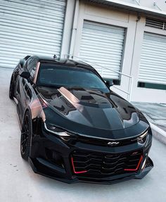 a black chevrolet camaro is parked in front of a garage with shutters open