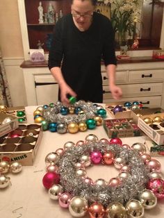 a man standing in front of a table filled with christmas balls and other ornaments on it