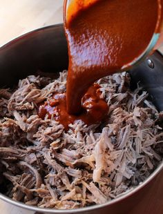 someone pouring sauce on shredded meat in a pot