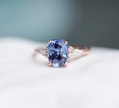 a tan and blue ring sitting on top of a white cloth with diamonds around it