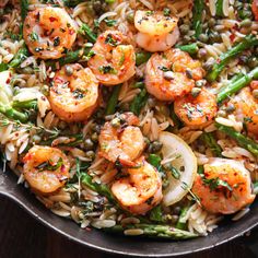 a skillet filled with shrimp, rice and asparagus on top of a wooden table