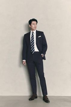 a man in a suit and tie leaning against a wall with his hands on his hips