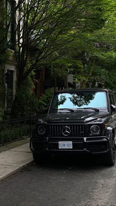 a black car parked on the side of a road next to a tree filled street