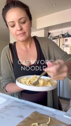 a woman holding a plate of food in front of her face with the words carnivore noodles on it