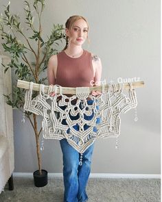 a woman standing next to a small tree holding a crocheted piece of clothing