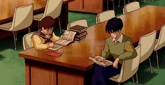 two people sitting at a table with books and papers in front of them on the floor