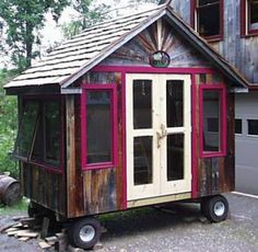 a small wooden house sitting in the middle of a parking lot next to a garage