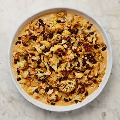 a white bowl filled with food on top of a marble countertop next to a knife and fork