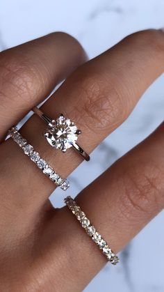 a woman's hand with three different rings on top of her ring and the middle one has an oval shaped diamond