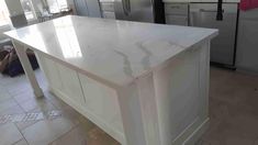 a large white kitchen island in the middle of a tile floored room with stainless steel appliances