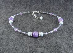 a purple and white beaded bracelet with beads on it's end, sitting on a gray surface