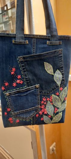 a pair of blue jeans with embroidered flowers and leaves are hanging from a metal pole