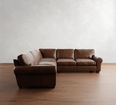 a brown leather couch sitting on top of a wooden floor next to a white wall