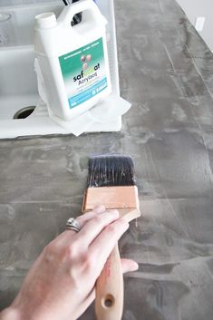 a person using a brush to clean a counter top with cement on the ground next to it