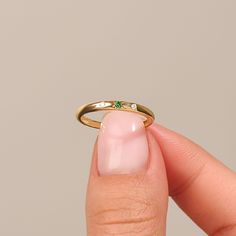 a woman's hand holding a gold ring with green stones