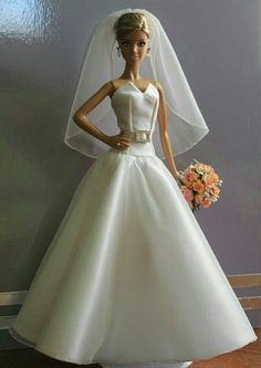 a barbie doll wearing a wedding dress and veil with flowers in her hand on a table