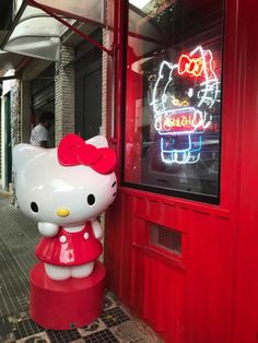 a hello kitty statue in front of a red building with neon signs on the windows