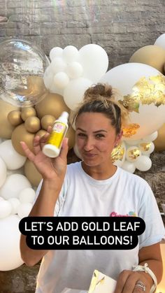 a woman holding up a bottle of gold leaf to her face with balloons in the background