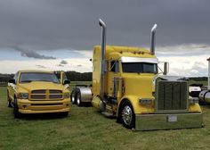 two large yellow trucks parked next to each other on a lush green grass covered field