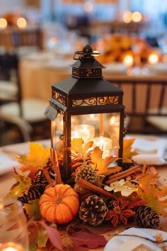 a lantern on top of a table filled with autumn leaves and pineconi cones