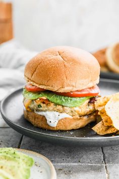 a chicken sandwich with lettuce and tomato on a plate next to some chips