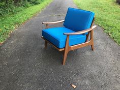 a blue chair sitting on the side of a road next to a lush green field