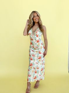 a woman standing in front of a yellow wall wearing a white dress with flowers on it