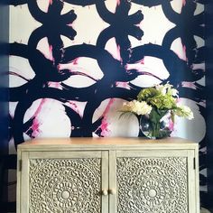 a vase with flowers sitting on top of a wooden cabinet in front of a painted wall